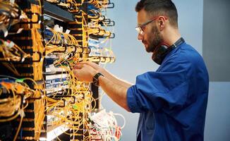 Side view. Young, man, is working with internet equipment and wires in server room photo