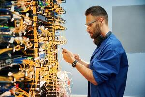Side view. .Young man is working with, internet equipment and wires in server room photo