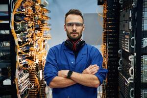 Standing with arms crossed. Young man is working with internet equipment and wires in server room photo
