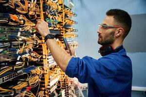 Side view. Young man is ,working with, internet equipment and wires in server room photo