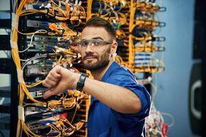 Showing, thumb down. Young man is working with internet equipment and wires in server room photo