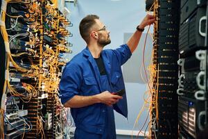 Cutting the wire. Young man is working ,,with internet equipment in server room photo