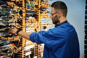Restoring, the, internet connection. Young man is working with equipment and wires in server room photo