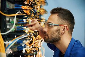 Looking, extremely close at cables. Young man is working with internet equipment and wires in server room photo