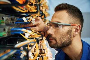 Looking extremely, close at cables. Young man is working with internet equipment and wires in server room photo