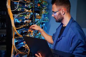 Cables management. Young man, is ,working with internet equipment and wires in server room photo