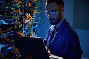 In glasses. Young, man ,is working with internet equipment and wires in server room photo
