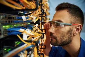 Looking extremely close at cables.,. Young man is working with internet equipment and wires in server room photo