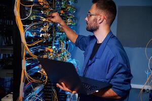 Cables management. Young man is ,working with internet equipment and wires in server room photo