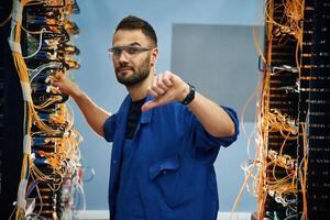 Showing thumb ,down. Young man is working with internet equipment and wires in server room photo