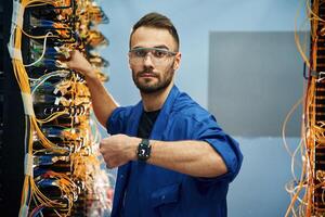 Showing watch. Young man is working with internet equipment and wires in server room photo