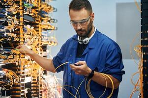 Modern, technology ,routing. Young ,man is working with internet equipment and wires in server room photo