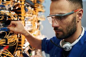Modern,, technology routing. Young man is working with internet equipment and wires in server room photo