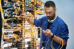 Administrator,, is busy. Young man is working with internet equipment and wires in server room photo