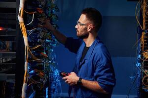 Blue, colored, lighting. Young man is working with internet equipment and wires in server room photo