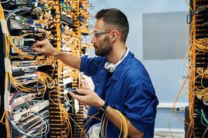 Modern, technology ,routing. Young man is working with internet equipment and wires in server room photo