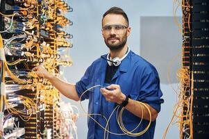 Checking signal ,by ,device. Young man is working with internet equipment and wires in server room photo
