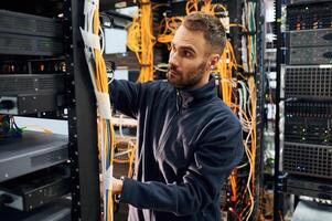 Black clothes.., Young man is working with internet equipment and wires in server room photo