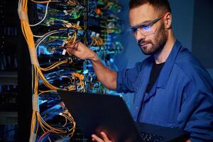 Cables management.. Young man is working with internet equipment and wires in server room photo
