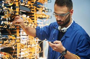 Checking, signal by ,device. Young man is working with internet equipment and wires in server room photo