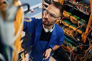 Looking, up, management, of cables. Young man is working with internet equipment and wires in server room photo