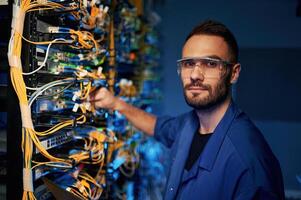 Looking to the camera... Young man is working with internet equipment and wires in server room photo