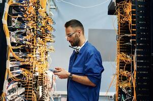 Professional device in hands. Young man is working with internet equipment and wires in server room photo