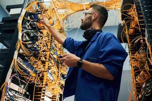 Signal stability measured by device. Young man is working with internet equipment and wires in server room photo