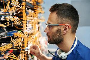 Modern technology, routing. Young man is working with internet equipment and wires in server room photo