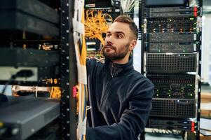 Black,clothes. Young man is working with internet equipment and wires in server room photo