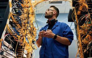 View from ,,below. Young man is working with internet equipment and wires in server room photo