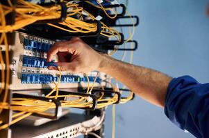 Close up view of hand that, fixing internet. Young man is working with equipment and wires in server room photo