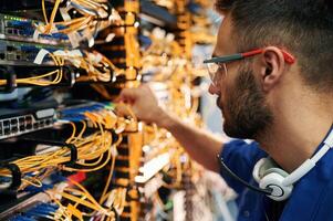 Modern, technology routing. Young man is working with internet equipment and wires in server room photo