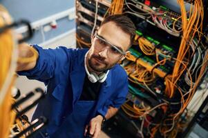 Looking up, management of cables.. Young man is working with internet equipment and wires in server room photo