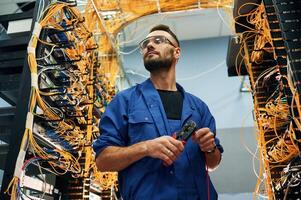 Administrator is busy,,. Young man is working with internet equipment and wires in server room photo