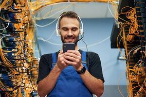 Headphones and ,smartphone. Young ,man is working with internet equipment and wires in server room photo