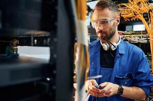 In blue ,colored, uniform. Young man is working with internet equipment and wires in server room photo