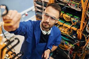 Looking up,,, management of cables. Young man is working with internet equipment and wires in server room photo