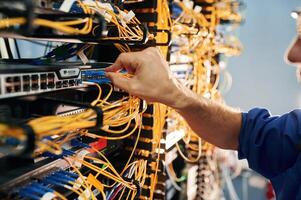 Close up ,view, of hand that fixing internet. Young man is working with equipment and wires in server room photo