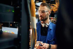 In blue,, colored uniform. Young man is working with internet equipment and wires in server room photo