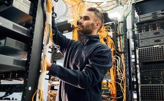 Black, clothes,. Young man is working with internet equipment and wires in server room photo