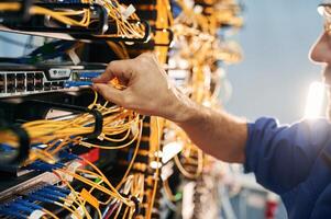 Close, up, view of hand that fixing internet. Young man is working with equipment and wires in server room photo