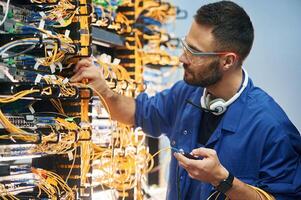 Checking ,signal by device. Young man is working with internet equipment and wires in server room photo
