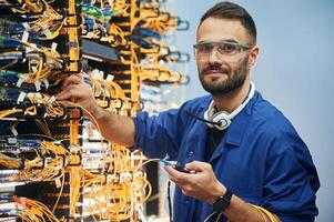 Checking ,signal by ,device. Young man is working with internet equipment and wires in server room photo