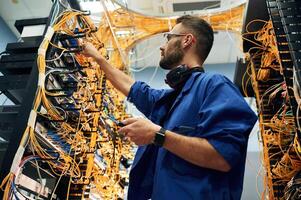 Signal ,,stability measured by device. Young man is working with internet equipment and wires in server room photo