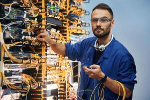 Looking to ,the camera. Young man is working with internet equipment and wires in server room photo