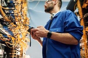 Professional device ,in hands. Young man is working with internet equipment and wires in server room photo