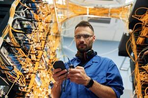 Professional, device in hands. Young man is working with internet equipment and wires in server room photo