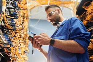 Professional device, in hands. Young man is working with internet equipment and wires in server room photo