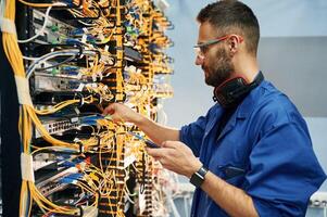 Signal ,stability measured by device. Young man is working with internet equipment and wires in server room photo